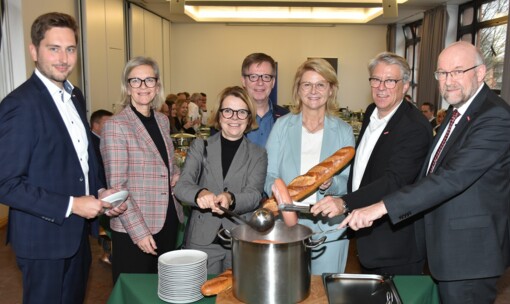 Handwerkspräsident, Kreishandwerkermeister, Geschäftsführer und drei Damen als Gäste stehen um einen Topf mit Würstchen und Brot